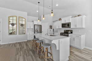 Kitchen with stainless steel appliances, light wood-style tile flooring, quartz countertops, a breakfast bar, and a center island with sink