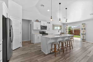 Kitchen featuring stainless steel appliances, light wood-style tile floors, quartz countertops, white cabinets, and vaulted ceiling