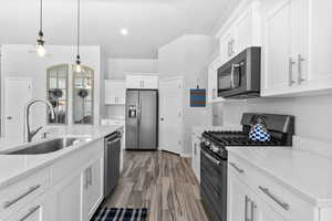 Kitchen featuring stainless steel appliances, white cabinets, quartz countertops, hanging light fixtures, wood-look tile floors, and recessed lighting