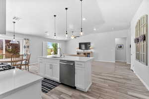 Kitchen with dishwasher, open floor plan, decorative light fixtures, quartz countertops, light wood-style tile flooring, and vaulted ceiling