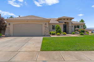 View of front facade with stucco siding, a front yard, an attached garage, and driveway
