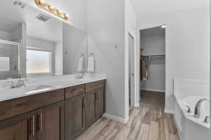 Primary Full bath featuring a shower stall, double vanity, a garden tub, a walk in closet, and wood-look tile floors