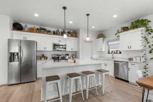 Kitchen featuring stainless steel appliances, light wood-style flooring, white cabinets, a breakfast bar area, and recessed lighting