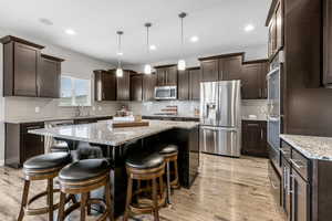Kitchen featuring stainless steel appliances, dark brown cabinets, a center island, light wood-style floors, and recessed lighting