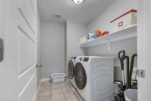 Laundry area with washing machine and clothes dryer, a textured ceiling, and light tile patterned flooring