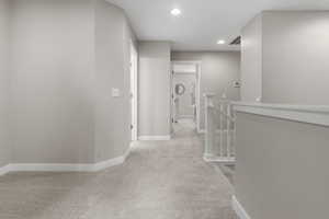 Hallway featuring an upstairs landing, light colored carpet, and recessed lighting