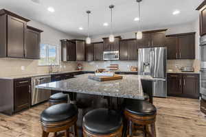 Kitchen with appliances with stainless steel finishes, dark brown cabinetry, a kitchen island, a breakfast bar, and recessed lighting