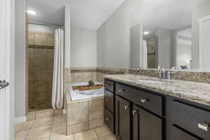 Bathroom featuring a garden tub, a tile shower, vanity, and tile patterned flooring