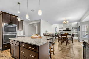 Kitchen featuring stainless steel double oven, light wood finished floors, a breakfast bar area, a center island, and dark brown cabinetry