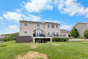 Rear view of house with a deck, roof mounted solar panels, and a lawn