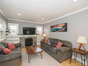 Living room with wood finished floors, crown molding, recessed lighting, and a fireplace