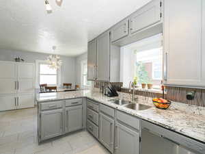 Kitchen with stainless steel dishwasher, gray cabinetry, a peninsula, light tile patterned flooring, and a textured ceiling