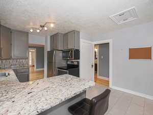 Kitchen featuring stainless steel appliances, a kitchen breakfast bar, a peninsula, light stone counters, and a textured ceiling