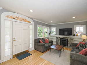 Living room with light wood-type flooring, ornamental molding, a premium fireplace, and recessed lighting