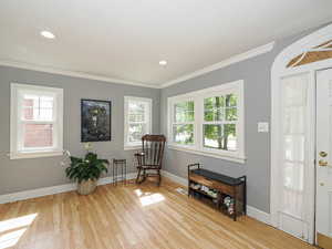 Living area with healthy amount of natural light, light wood finished floors, crown molding, and recessed lighting