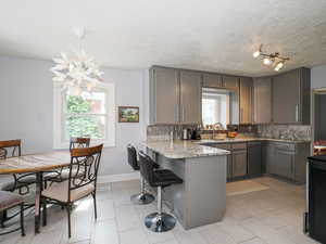 Kitchen with dishwashing machine, a peninsula, light stone counters, a breakfast bar, and a chandelier