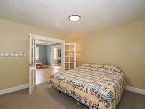 Carpeted bedroom featuring french doors and a textured ceiling