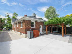 View of property exterior featuring a patio, brick siding, a chimney, and a shingled roof