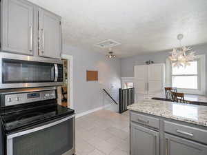 Kitchen with appliances with stainless steel finishes, gray cabinets, light tile patterned flooring, a textured ceiling, and light stone counters