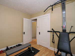 Exercise room with light wood-style floors and a textured ceiling