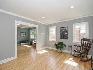 Living area with ornamental molding, light wood-style flooring, and recessed lighting