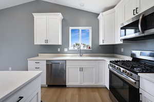 Kitchen with appliances with stainless steel finishes, light wood-style flooring, white cabinets, and lofted ceiling