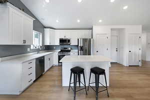 Kitchen featuring appliances with stainless steel finishes, a kitchen breakfast bar, a kitchen island, white cabinetry, and light wood-type flooring