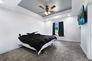 Carpeted bedroom with a tray ceiling, recessed lighting, and a ceiling fan