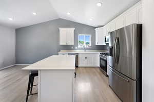 Kitchen with appliances with stainless steel finishes, light wood-type flooring, vaulted ceiling, a kitchen island, and a kitchen breakfast bar