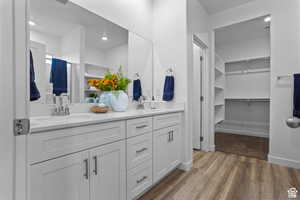 Bathroom featuring double vanity, wood finished floors, a walk in closet, and recessed lighting