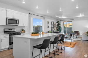 Kitchen with appliances with stainless steel finishes, a center island with sink, a breakfast bar area, wood finished floors, and recessed lighting