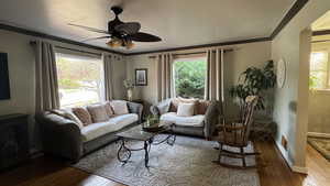 Living room featuring ornamental molding, dark wood-type flooring, and ceiling fan