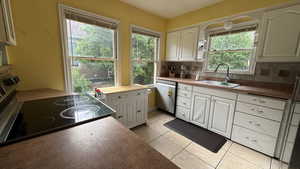 Kitchen featuring dishwasher, electric range, decorative backsplash, light tile patterned floors, and white cabinetry