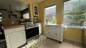 Kitchen featuring electric stove, a chandelier, light tile patterned floors, and white cabinetry