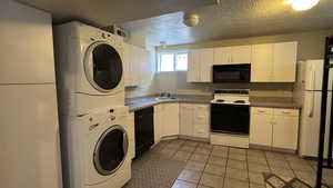 Kitchen with black appliances, stacked washer and clothes dryer, light tile patterned flooring, white cabinets, and a textured ceiling
