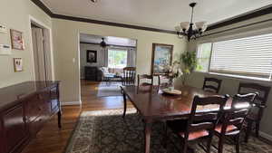 Dining space with healthy amount of natural light, dark wood-style floors, a chandelier, and crown molding