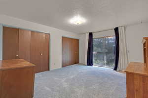 Unfurnished bedroom featuring access to outside balcony, carpet floors, two closets, and a textured ceiling