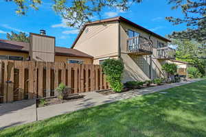 Back of property with a balcony and fenced patio.