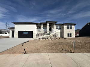 View of front of home with stone siding, a garage, concrete driveway, and covered porch