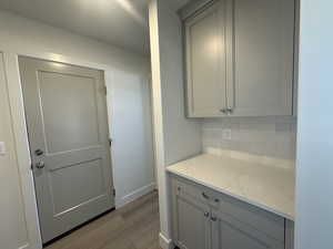 Kitchen with gray cabinetry, decorative backsplash, wood finished floors, and light stone countertops