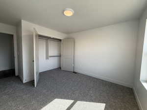 Unfurnished bedroom with dark colored carpet, a closet, and a textured ceiling