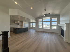 Unfurnished living room featuring a fireplace, light wood-style floors, ceiling fan, vaulted ceiling, and a textured ceiling