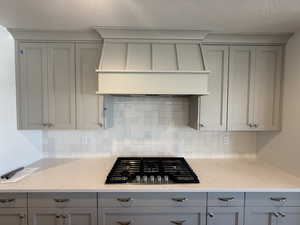 Kitchen with gray cabinetry, gas stovetop, custom range hood, and a textured ceiling