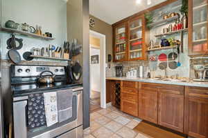 Kitchen featuring stainless steel electric range oven, backsplash, open shelves, light tile patterned flooring, and light countertops