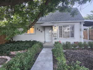 View of charming stucco facade, mature trees, low maintenance landscaping, and carport