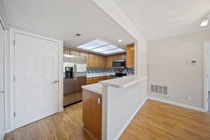 Kitchen with appliances with stainless steel finishes, light wood-type flooring, brown cabinetry, a peninsula, and recessed lighting
