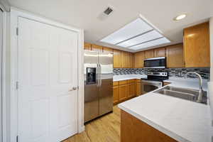 Kitchen with appliances with stainless steel finishes, brown cabinets, light countertops, light wood-type flooring, and backsplash
