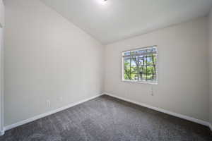 Spare room featuring dark colored carpet and lofted ceiling