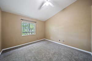 Carpeted spare room featuring vaulted ceiling and ceiling fan
