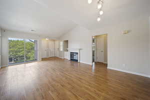 Unfurnished living room featuring light wood-style flooring, a glass covered fireplace, and lofted ceiling